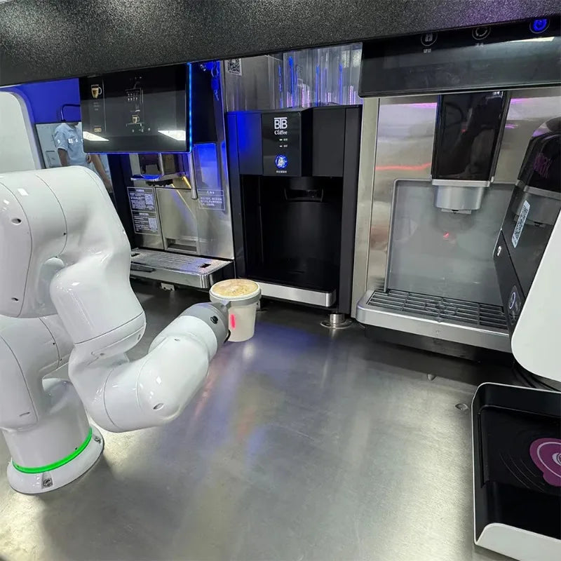 Robot barista con brazo blanco y dispensadores, dentro de cabina de servicio