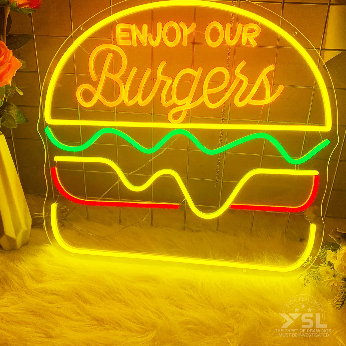 Letrero de neón con texto 'ENJOY OUR Burgers' y formas de hamburguesa, amarillo y rojo.