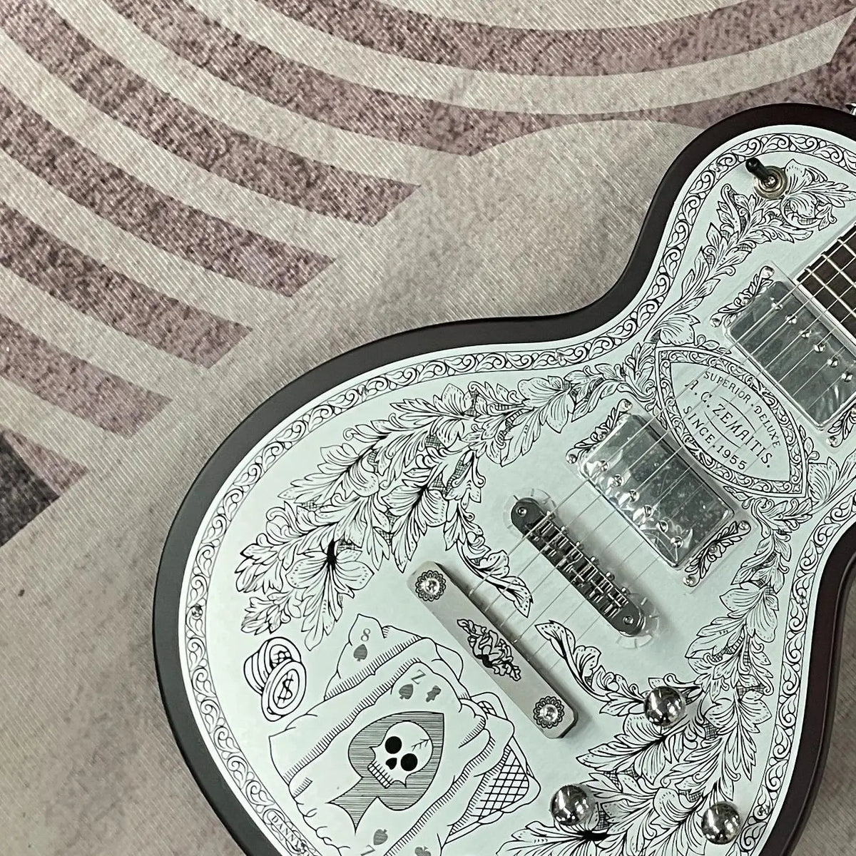 Guitarra eléctrica con tapa de aluminio grabado, cuerpo de caoba, incrustaciones de ébano en la tapa, doble sistema de pastillas humbucker, puente fijo cromado, 22 trastes.