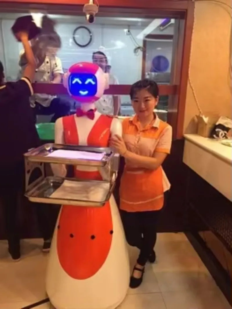 Robot camarero blanco con traje rojo y bandeja metálica, junto a una persona