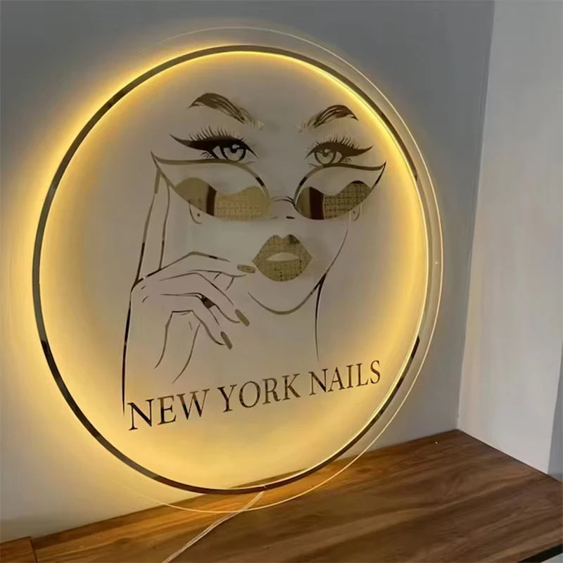 Letrero circular LED de acrílico con logo de rostro y texto «NEW YORK NAILS», luz cálida.