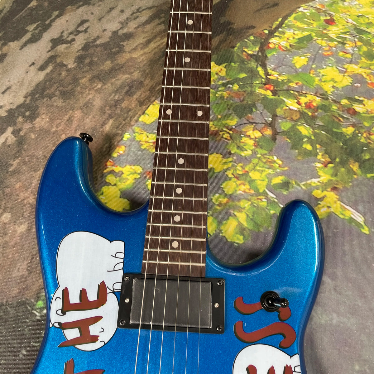 Guitarra eléctrica con grafiti en fondo azul, doble pastilla de alta ganancia, sistema de doble tremolo, guitarra eléctrica para speed picking.