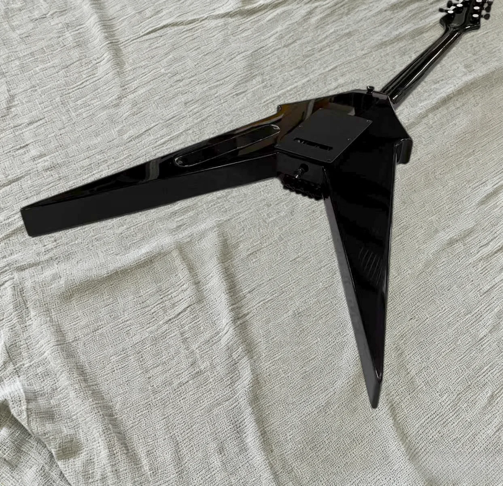 Guitarra eléctrica con forma de V, diseño geométrico en color plateado y negro, placa frontal de aluminio, puente con sistema de trémolo, pastillas HH, herrajes negros.