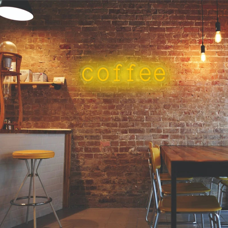 Letrero LED de neón con texto “coffee” en luz amarilla sobre ladrillo.