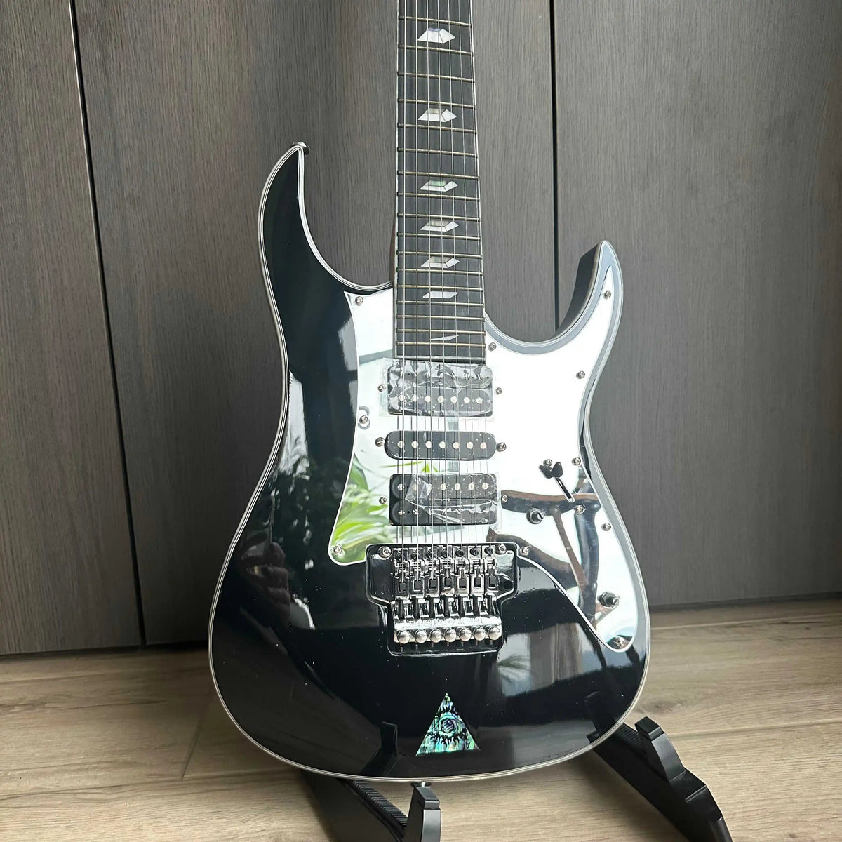 Guitarra eléctrica de 7 cuerdas, de color negro, con protector de cuerdas tipo espejo, pastillas HSH y puente con trémolo, ideal para guitarristas avanzados.