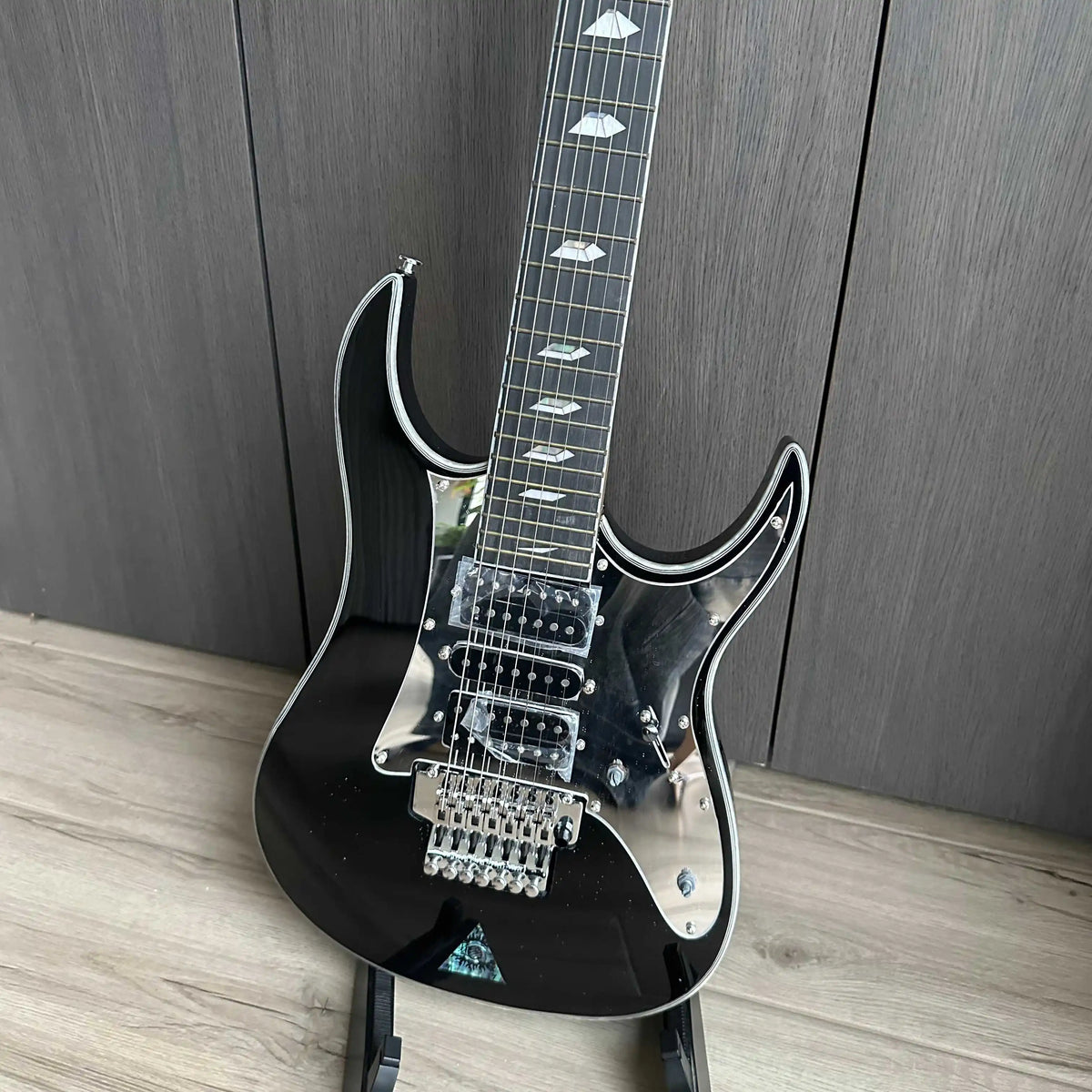 Guitarra eléctrica de 7 cuerdas, de color negro, con protector de cuerdas tipo espejo, pastillas HSH y puente con trémolo, ideal para guitarristas avanzados.