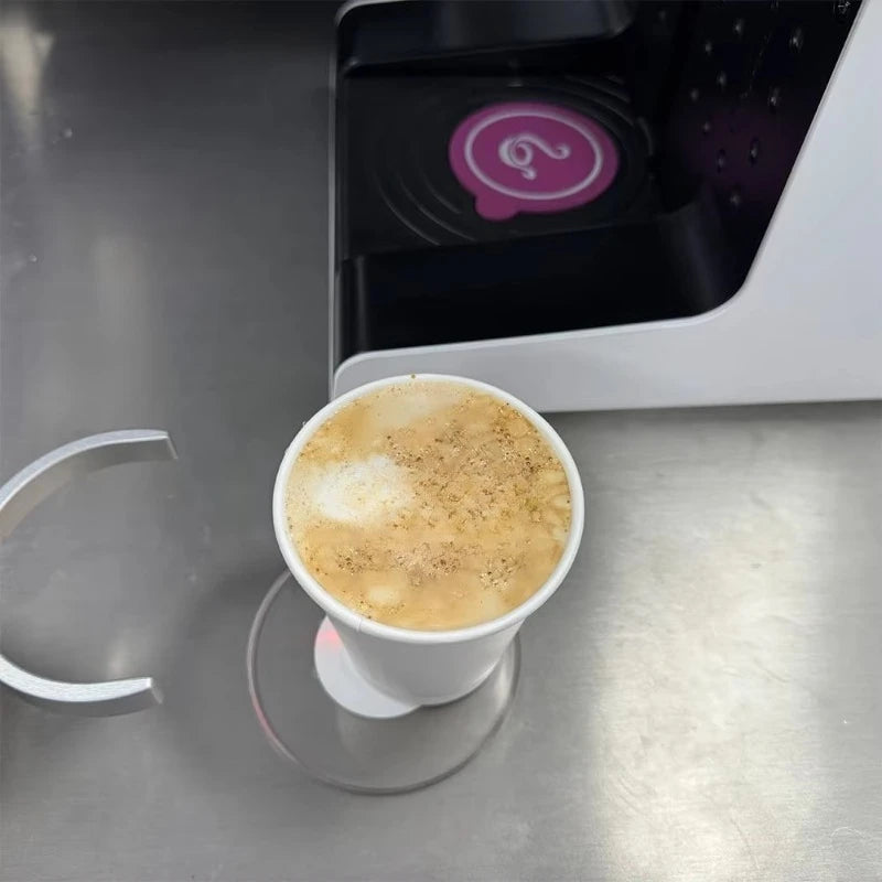 Taza de café sobre superficie metálica con boquilla del robot barista