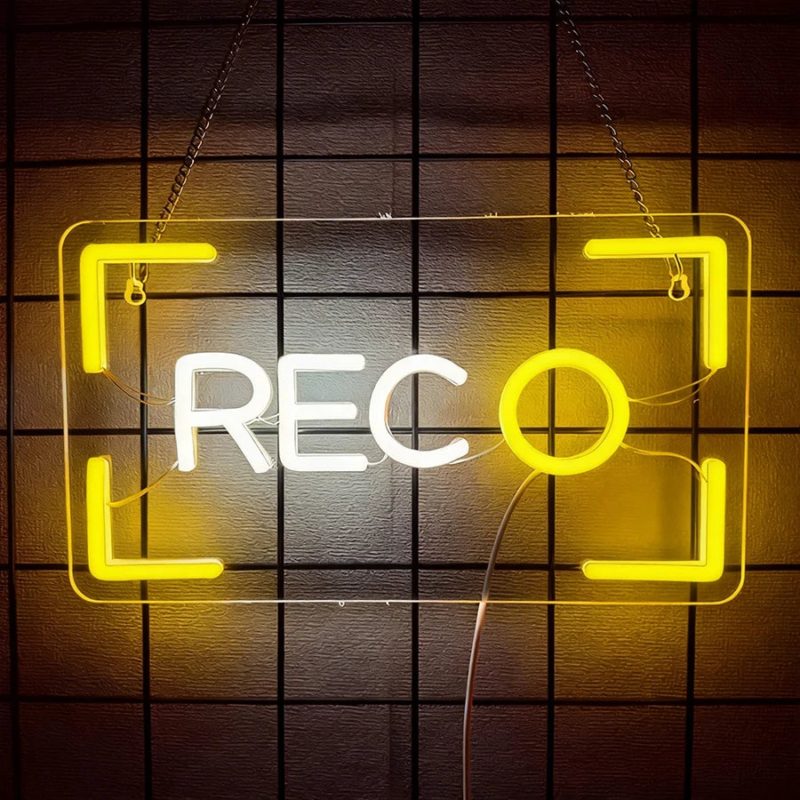 Letrero LED neón tipo cámara REC con marco amarillo y letras blancas, colgado con cadena