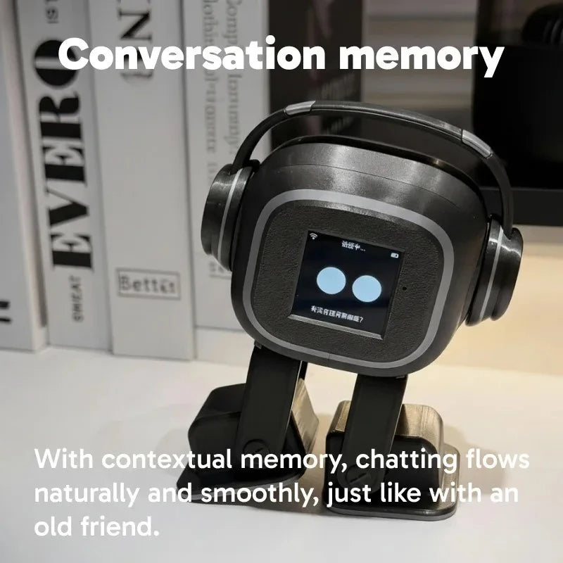 Robot de escritorio gris y negro con auriculares, pantalla con dos luces azules sobre libros.