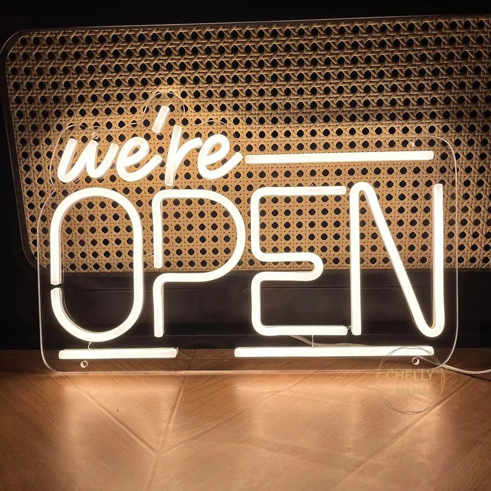 Letrero de neón LED “We’re OPEN” iluminado, letras blancas sobre placa transparente