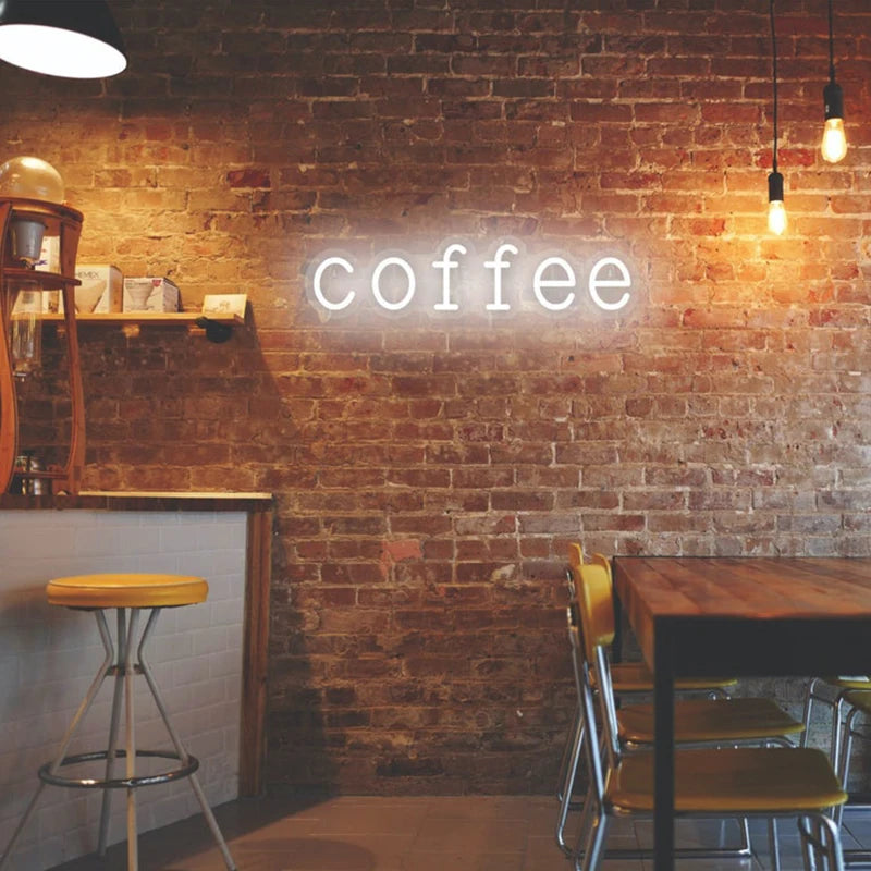 Letrero LED de neón con texto “coffee” en luz blanco cálido sobre ladrillo.